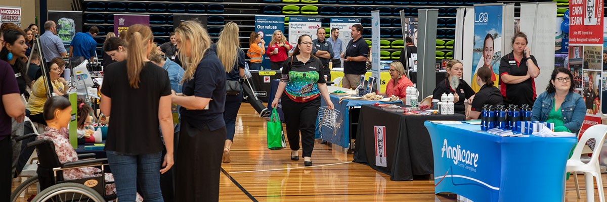 Job seekers are walking down a row of tables where health organisations work at employment booths