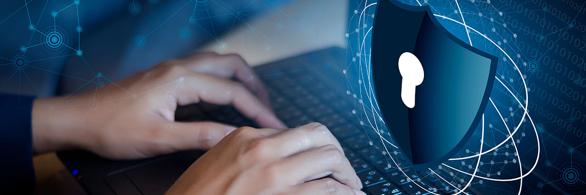 A person is typing on a laptop in a dark room with a superimposed shield bursting from the screen