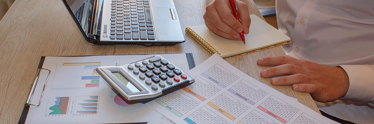 A man is sitting at a desk with a calculator, pen and paper reviewing financial business documents