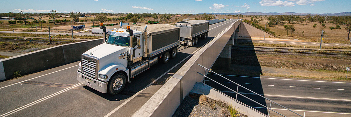 A truck is driving across a highway overpass, carrying two trailer loads of product for export