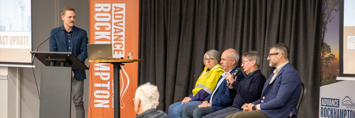 Four people sitting on stage for a panel discussion. One person is speaking into a microphone addressing a crowd.