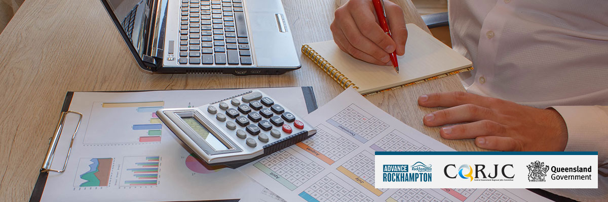 A man is sitting at a desk with a calculator, pen and paper reviewing financial business documents